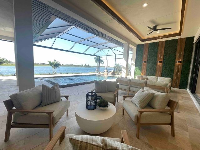 inside a lanai area of a custom home in wellen park. Large windows look out to the pool view, while neutral coloured furniutre circle a small white table with a lantern on top. 
