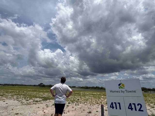 wide open space building lot in wellen park. Grey clouds overhead, nd Josh stands next to sign saying "Homes by Towne, 411, 412, available now"
