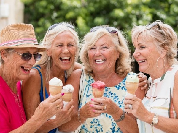 four women stand huddled in a row together smiling, each holds an ice cream cone