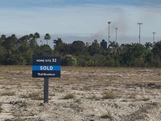 a blue sold sign is planted in the empty building lot for home construction