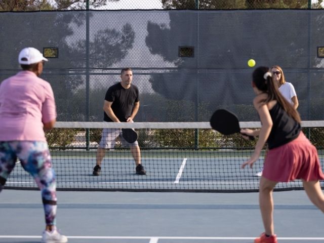 a pickleball court is fenced in and two teams of doubles are in position ready to play picklkeball