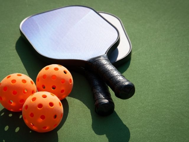 black pickleball bat and orange balls laying on a green court floor