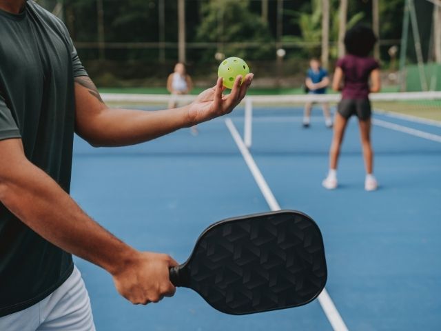 man holding a black pickleball bat about to serve across the blue court