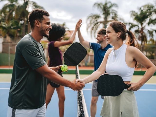 two women and two men reach over a pickleball cout net to shake hands and high-five each other. it's a great display of the kind of team spirit shown when people play pickleball in venice florida