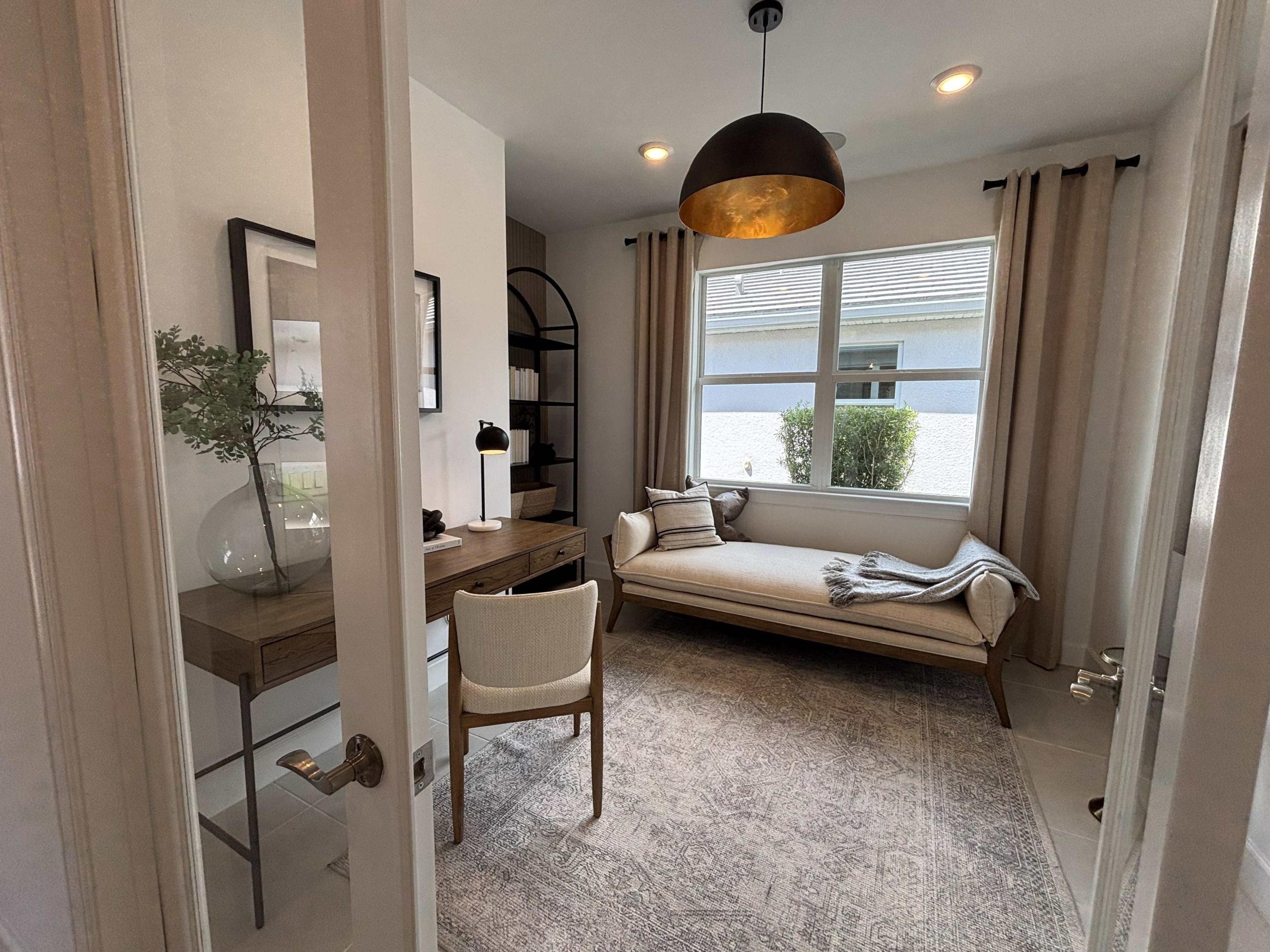 flex room in neutral colors and large bright window behind a sofa and desk