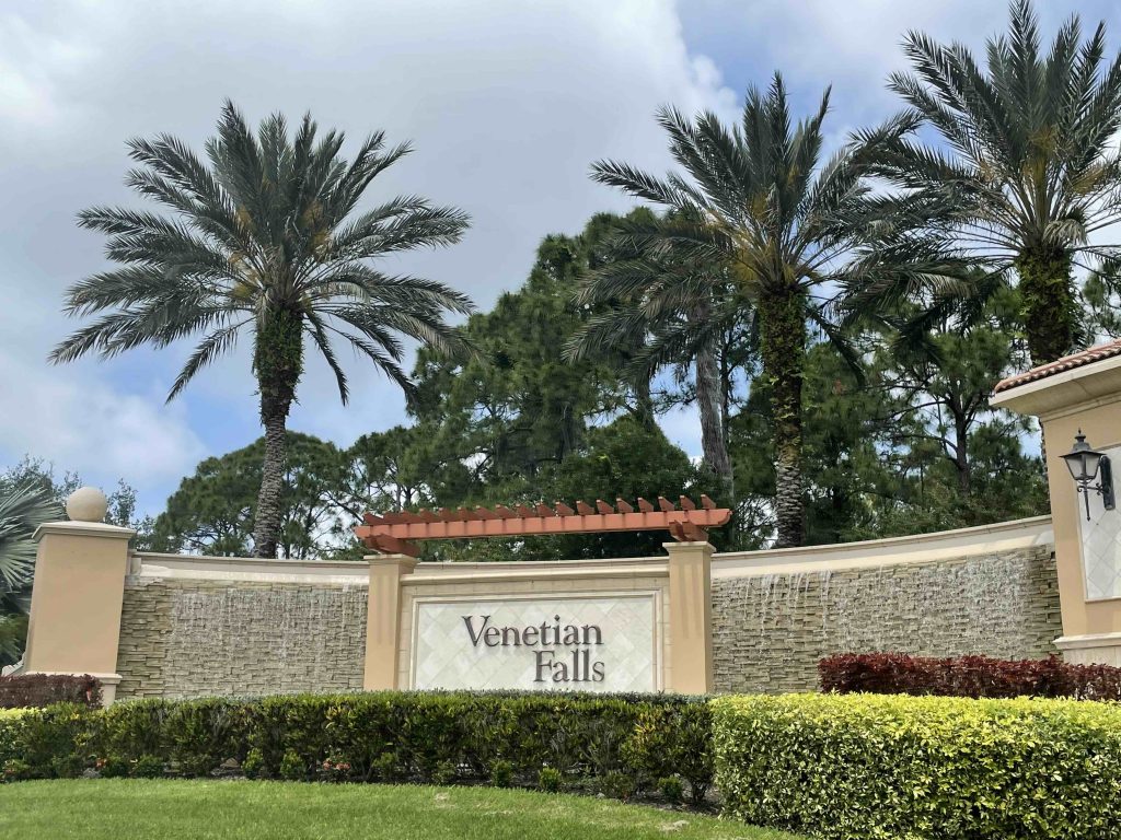 entrance sign to venetian falls, which has no cdd fees. palm trees line the sky behind the sign. 