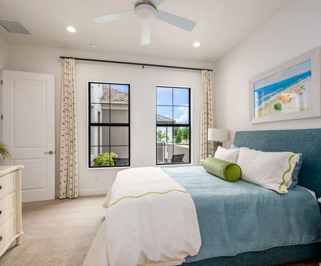 crisp stylish bedroom in whites and blues for a fresh feel. two large windows are on the wall facing us, and the bed sits perpendicular with large matching throws.