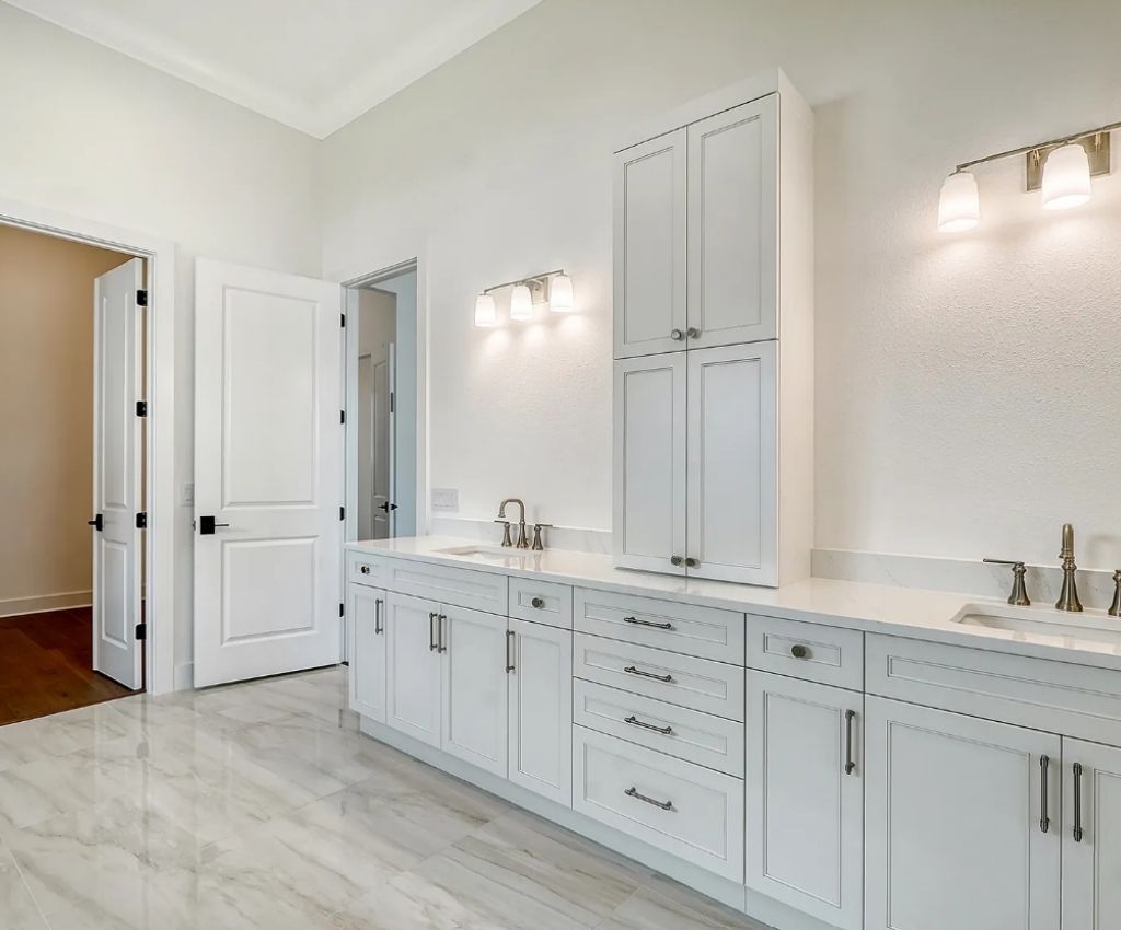 white gloss cupboards line the wall of the spacious bathroom, with sleek chrome handles and overhead spotlights.