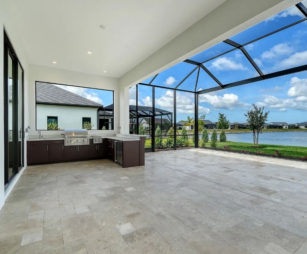 outdoor lanai area with clear tiled floor, dark wood grill area in the corner for outdoor cooking and dining, and a large pool to the side with glass roof covering it.
