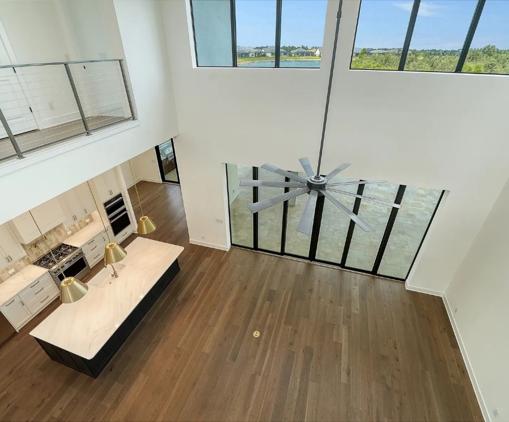 birds eye view from the mezanine over the main living and kitchen areas, showing the dark hardwood floors, large windows with lots of natural light, and sleek white counter tops.